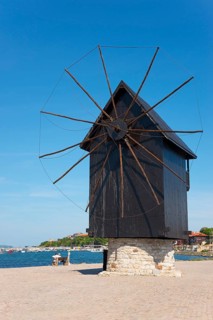 Close-up of a historic windmill on the dam in front of a bright blue sky by the sea, landmark,