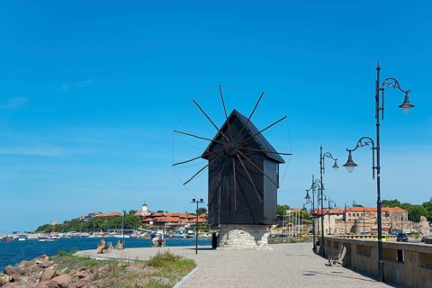 Traditional windmill on the embankment on a sunny day on the coastal promenade with blue sky,