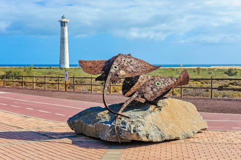 In the foreground sculpture made of scrap metal of marine animals two stingrays rays on stone