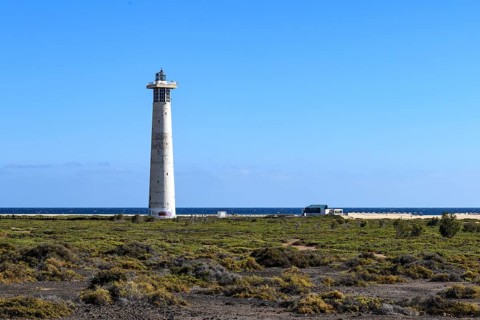 View of lighthouse Faro de Morro Jable on east coast of peninsula Jandia, in the foreground green