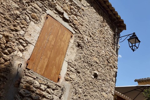 Facades of old sandstone houses with shutters and a street lamp in Goudargues, Departement Gard,