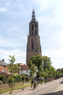 Woman cycling by Gothic church clock tower, Onze Lieve Vrouwetoren, Amersfoort, Netherlands
