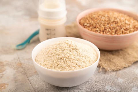 Powdered milk and buckwheat baby food mix, infant formula, pacifier, bottle, spoon on brown