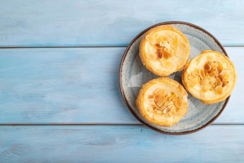 Traditional portuguese cakes pasteis de nata, custard small pies with almonds on blue wooden