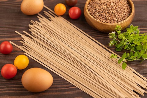 Japanese buckwheat soba noodles with tomato, eggs, spices, herbs on brown wooden background. Side