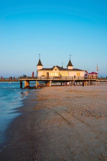 People strolling on a pier with buildings in the sunset, clear, blue, cloudless sky, pier Ahlbeck