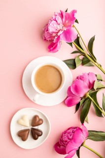 Cup of cioffee with chocolate candies, pink peony flowers on pink pastel background. top view, flat