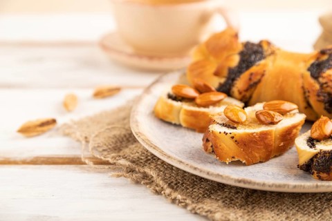 Homemade sweet bun with honey almonds and cup of green tea on a white wooden background and linen