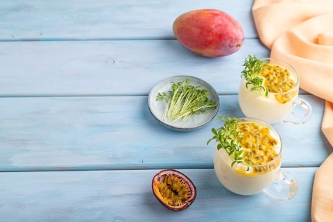 Mango yogurt with passionfruit and cilantro microgreen in glass on blue wooden background with