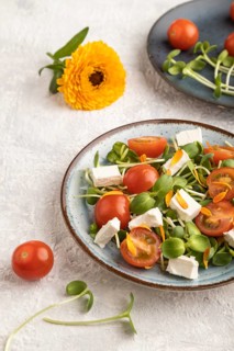 Vegetarian vegetables salad of tomatoes, marigold petals, microgreen sprouts, feta cheese on gray
