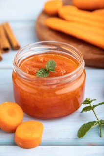 Carrot jam with cinnamon in glass jar on blue wooden background. Side view, close up, selective