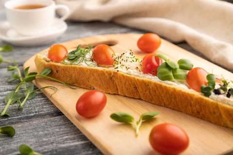 Long white bread sandwich with cream cheese, tomatoes and microgreen on gray wooden background and
