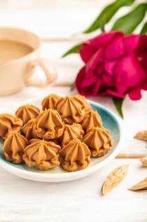Homemade soft caramel fudge candies on blue plate and cup of coffee on gray concrete background,