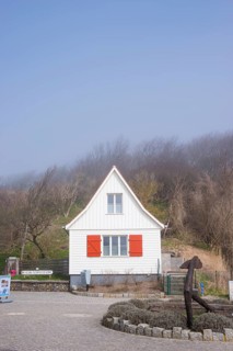Old, white wooden house with red shutters stands in the fog, old anchor, sea fog, wind fugitive,