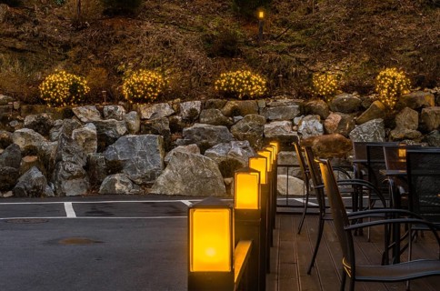 Yellow lights on patio banister with small evergreen shrubs decorated with Christmas lights in