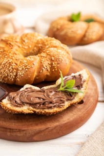 Homemade sweet bun with chocolate cream and cup of coffee on a white wooden background and linen