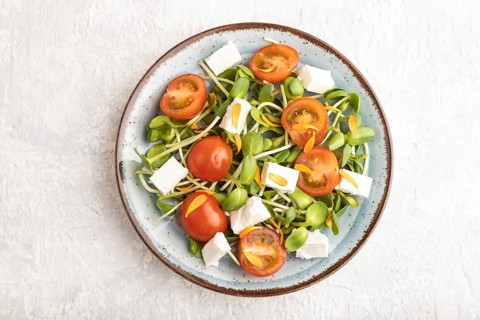 Vegetarian vegetables salad of tomatoes, marigold petals, microgreen sprouts, feta cheese on gray