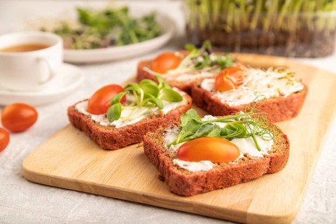 Red beet bread sandwiches with cream cheese, tomatoes and microgreen on gray concrete background.