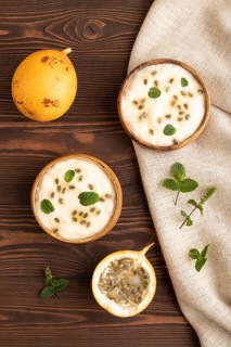 Yoghurt with granadilla and mint in wooden bowl on brown wooden background and linen textile. top