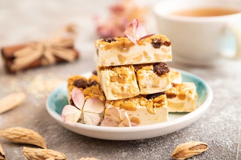 Traditional candy nougat with nuts and sesame with cup of green tea on brown concrete background.