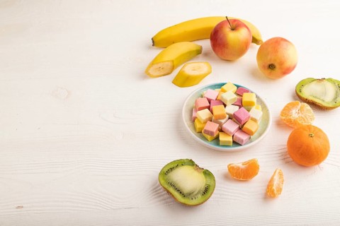 Various fruit jelly chewing candies on plate on white wooden background. apple, banana, tangerine,