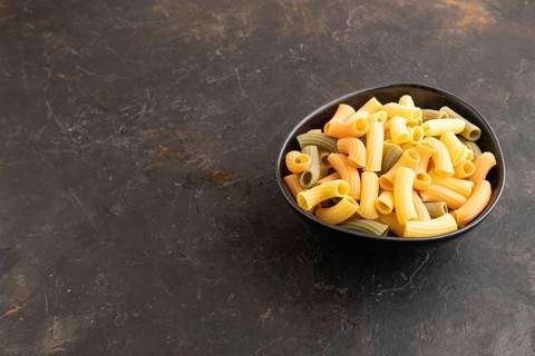 Rigatoni colored raw pasta with tomato, eggs, spices, herbs on black concrete background. Side