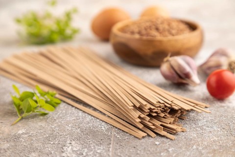 Japanese buckwheat soba noodles with tomato, eggs, spices, herbs on brown concrete background. Side