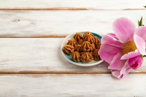 Homemade soft caramel fudge candies on blue plate on white wooden background, peony flower
