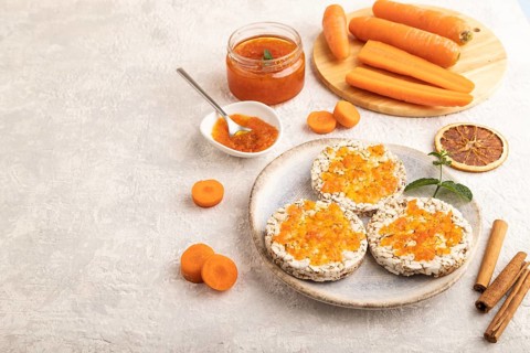 Carrot jam with puffed rice cakes on gray concrete background. Side view, copy space