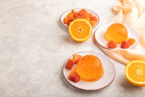 Papaya and orange jelly on gray concrete background and orange linen textile. side view, flat lay,