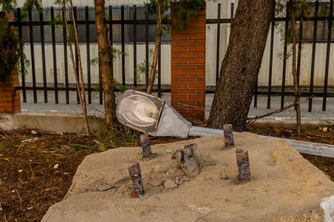 Old dismantled streetlight removed from lamppost and laying on ground behind concrete streetlamp