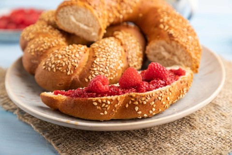 Homemade sweet bun with raspberry jam and cup of coffee on a blue wooden background and linen