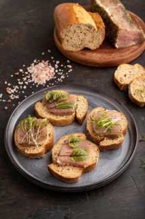 Bread sandwiches with jerky salted meat, sorrel and cilantro microgreen on black concrete