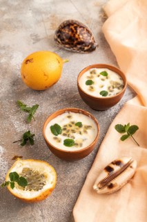 Yoghurt with granadilla and mint in clay bowl on brown concrete background and orange linen textile