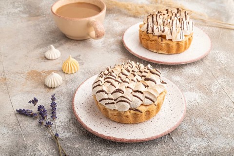 Two tartlets with meringue cream and cup of coffee on brown concrete background. side view.