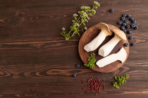 King Oyster mushrooms or Eringi (Pleurotus eryngii) on brown wooden background with blueberry,