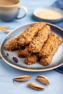 Crumble cookies with seasme and almonds on ceramic plate with cup of coffee and blue linen textile