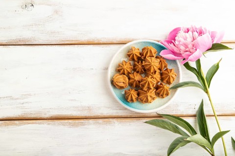 Homemade soft caramel fudge candies on blue plate on white wooden background, peony flower
