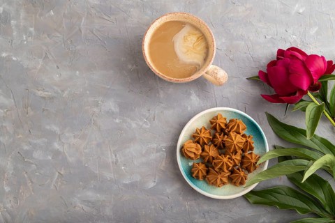 Homemade soft caramel fudge candies on blue plate and cup of coffee on gray concrete background,