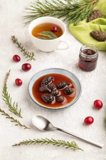 Pine cone jam with herbal tea on gray concrete background and green linen textile. Side view, close