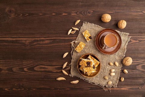 Traditional candy nougat with nuts and sesame with cup of green tea on brown wooden background and