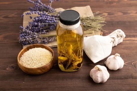 Sunflower oil in a glass jar with various herbs and spices, lavender, sesame, rosemary on a brown