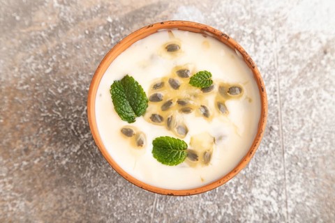 Yoghurt with granadilla and mint in clay bowl on brown concrete background. top view, flat lay,