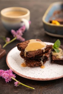 Chocolate brownie with caramel sauce with a cup of coffee on black concrete background. side view,