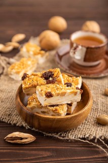 Traditional candy nougat with nuts and sesame with cup of green tea on brown wooden background and