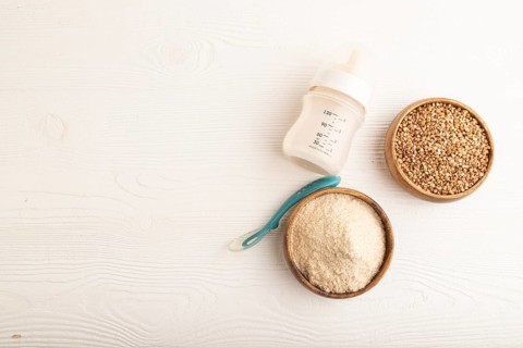 Powdered milk and buckwheat baby food mix, infant formula, pacifier, bottle, spoon on white wooden