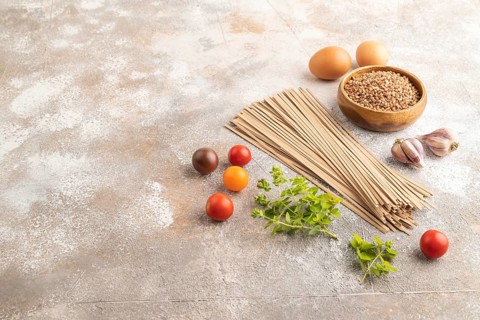 Japanese buckwheat soba noodles with tomato, eggs, spices, herbs on brown concrete background. Side