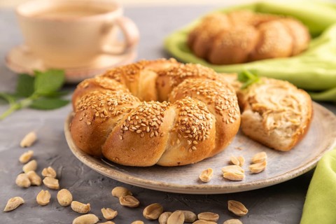 Homemade sweet bun with peanut butter and cup of coffee on a gray concrete background and green