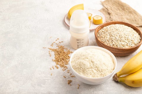 Powdered milk and oatmeal, banana baby food mix, infant formula, pacifier, bottle, spoon on gray