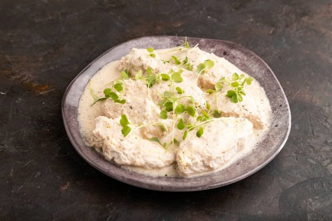 Stewed chicken fillets with coconut milk sauce and rucola microgreen on black concrete background.